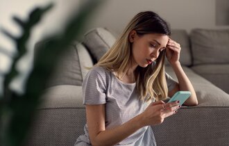 Ernste, nachdenkliche junge Frau mit Smartphone