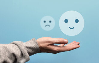 Über einer ausgestreckten Hand schweben ein fröhlicher und ein trauriger Smiley